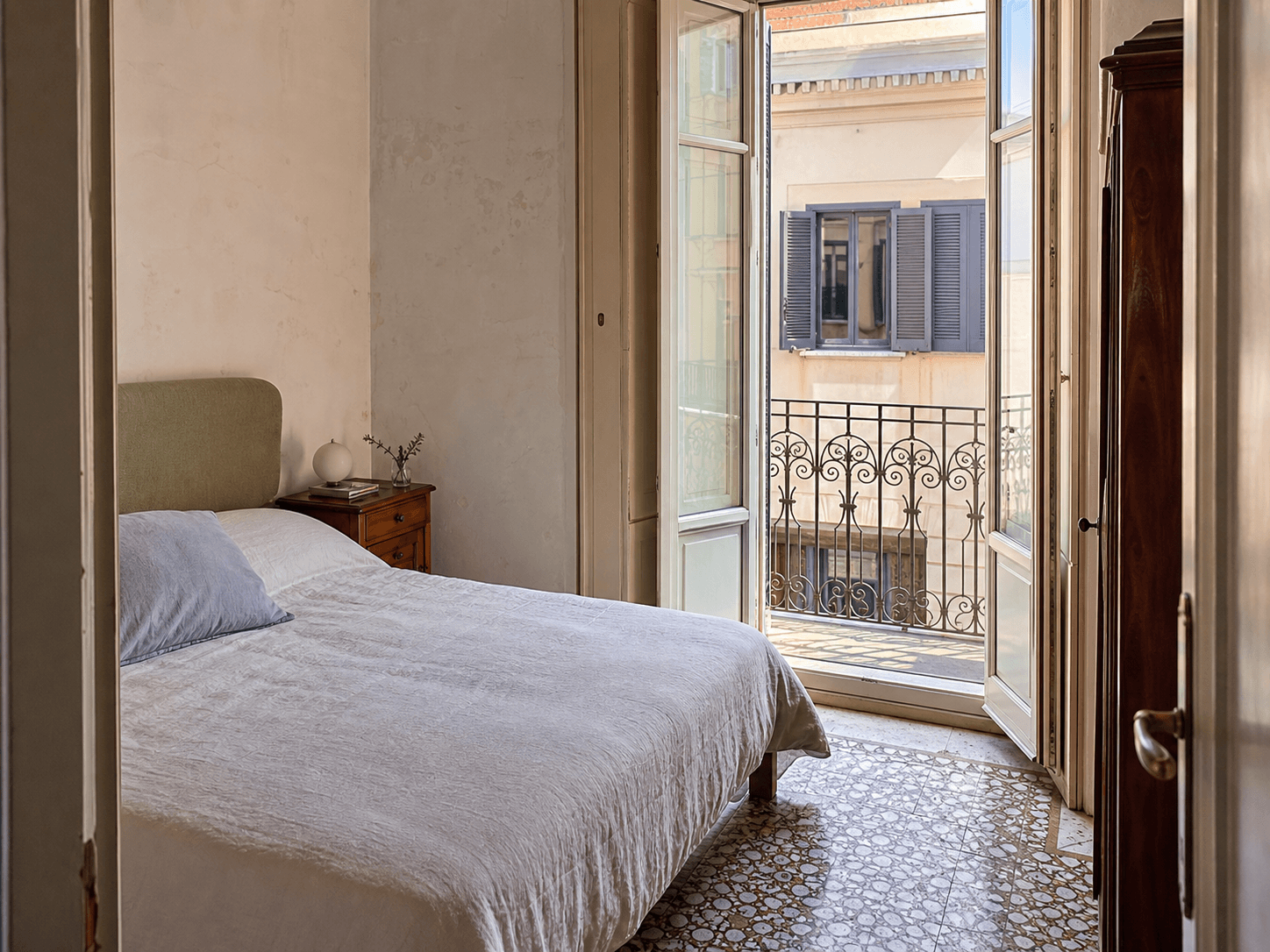 Camera di un appartamento italiano con letto in lino e balcone affacciato sui palazzi vicini